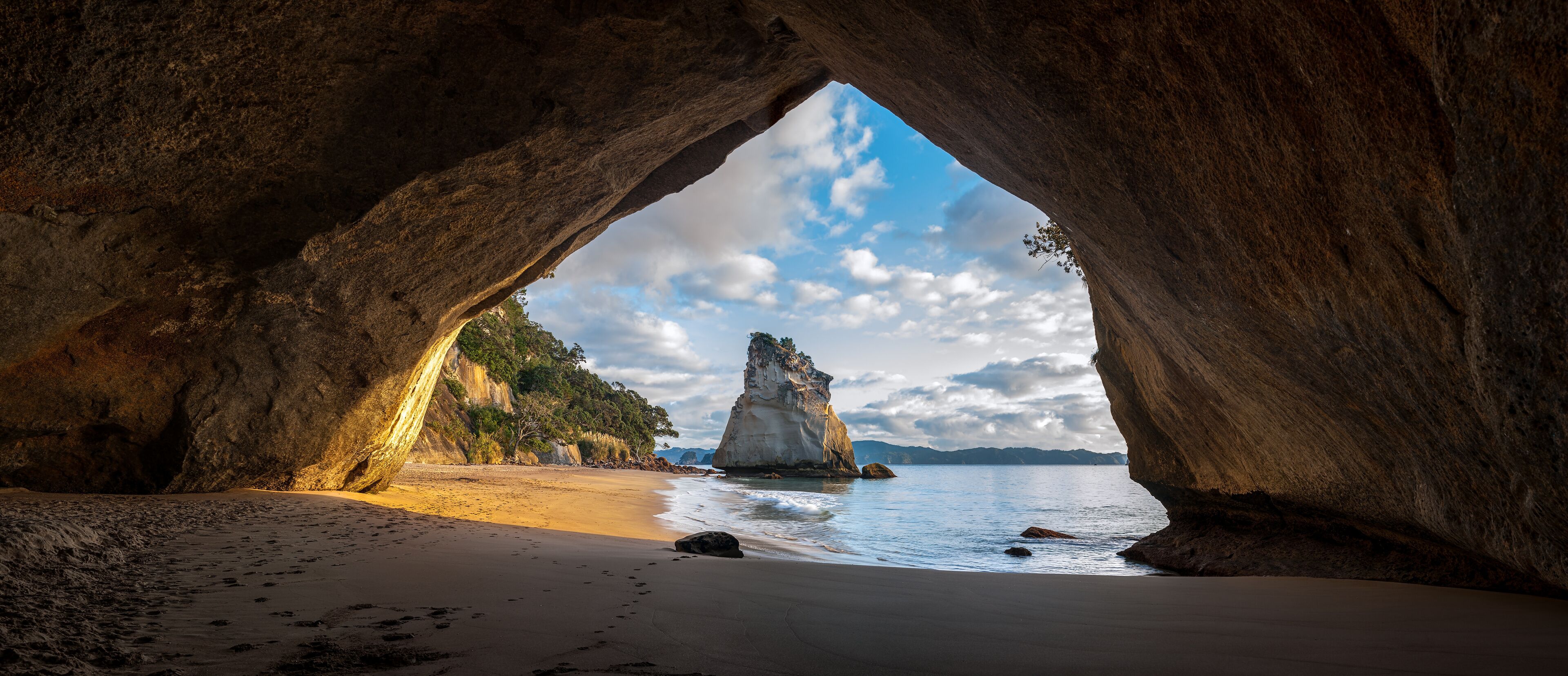 A natural rock arch over a beach with a prominent rock formation in the background.