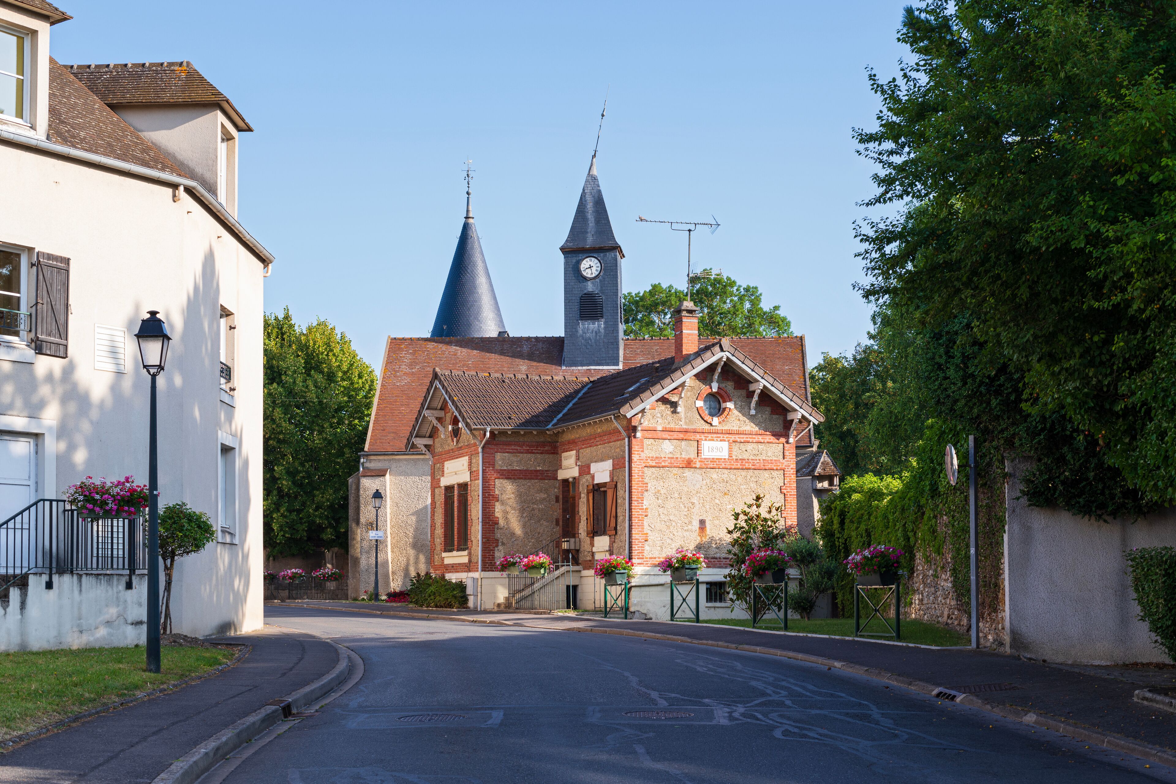 A quaint village street with a church featuring two spires and a clock tower.