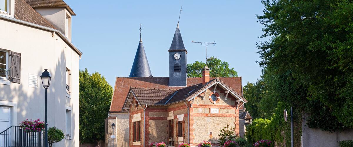 A quaint village street with a church featuring two spires and a clock tower.