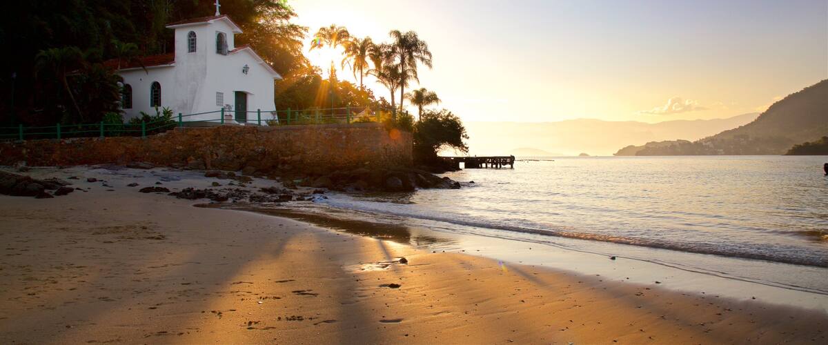 A beach with a white church, palm trees, and a pier extending into the water.