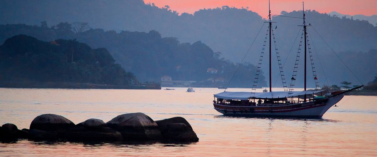 A boat on calm water with a sunset sky and hills in the background.