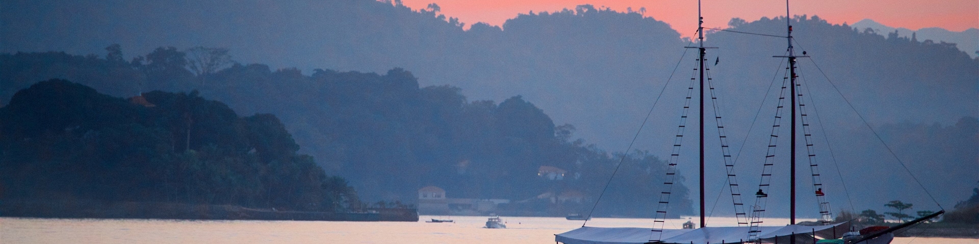 A boat on calm water with a sunset sky and hills in the background.