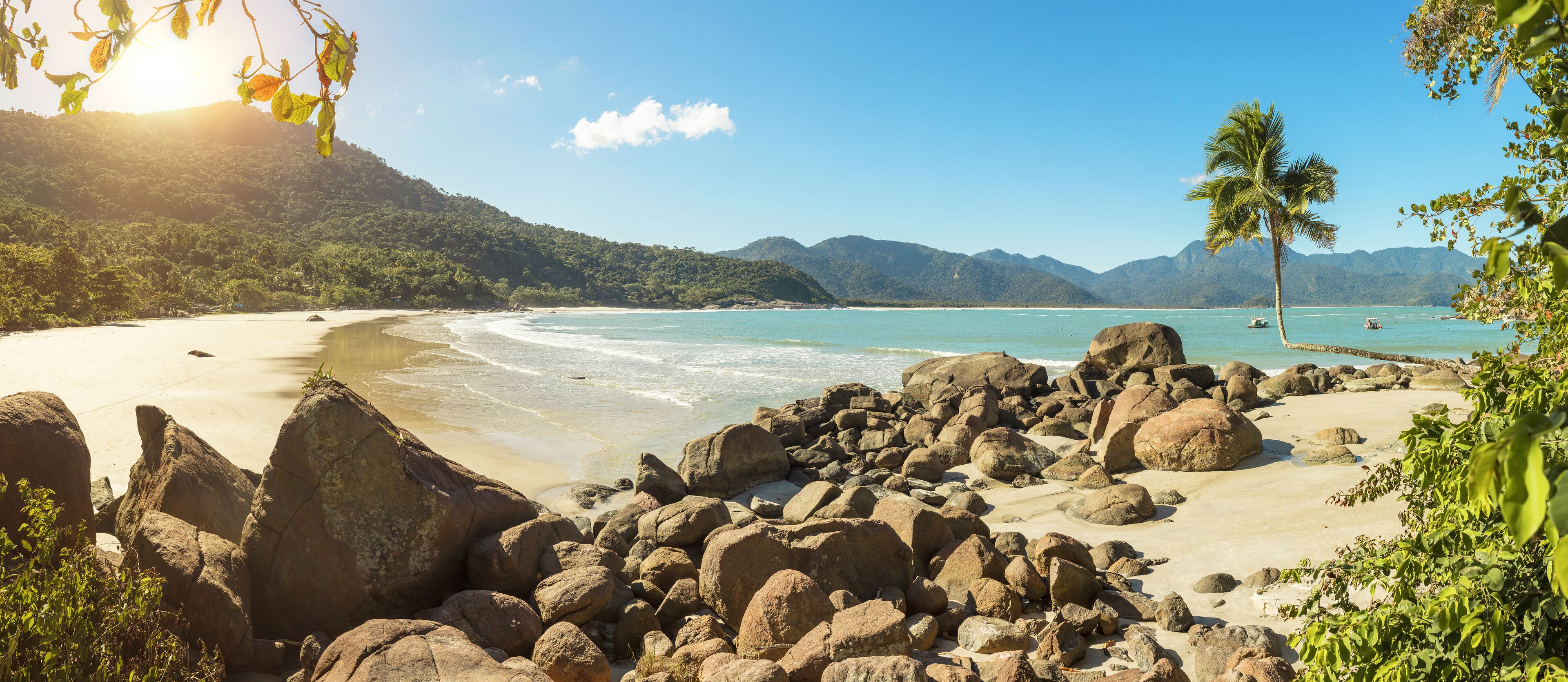 Una playa tropical con rocas grandes, agua turquesa cristalina y palmeras.