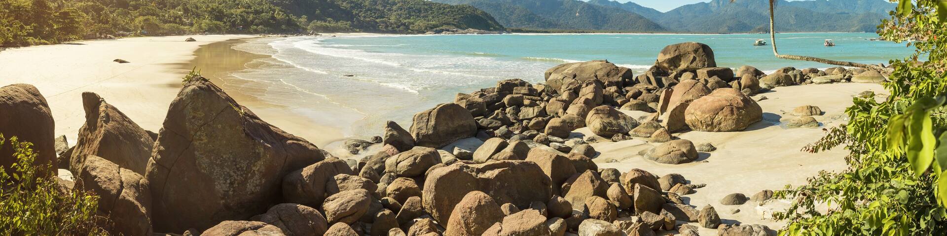 A tropical beach with large rocks, clear turquoise water, and palm trees.
