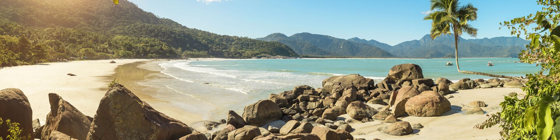 Una playa tropical con rocas grandes, agua turquesa cristalina y palmeras.