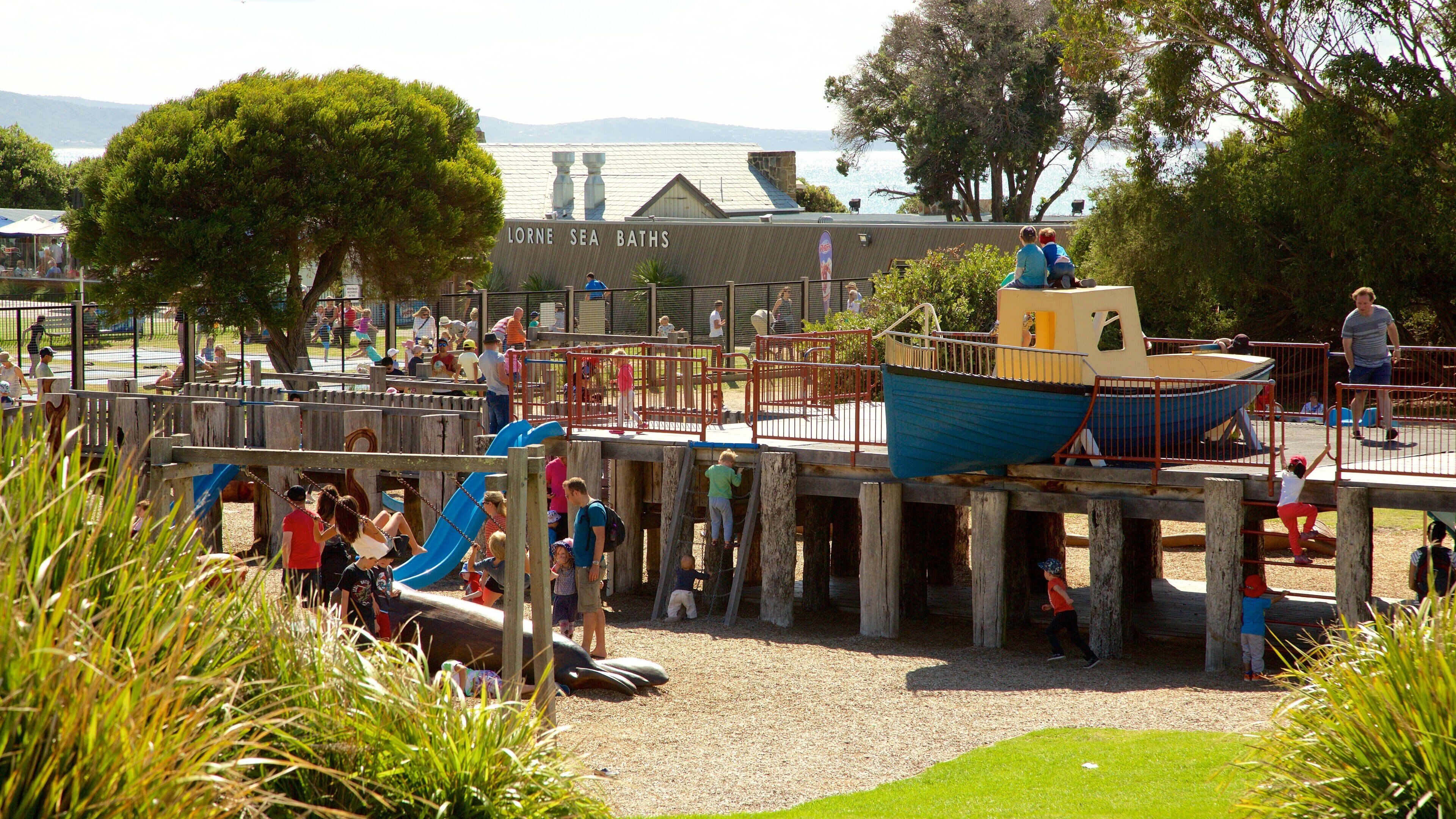 A playground with slides and climbing structures, a blue boat, and a sign reading "Lorne Sea Baths".