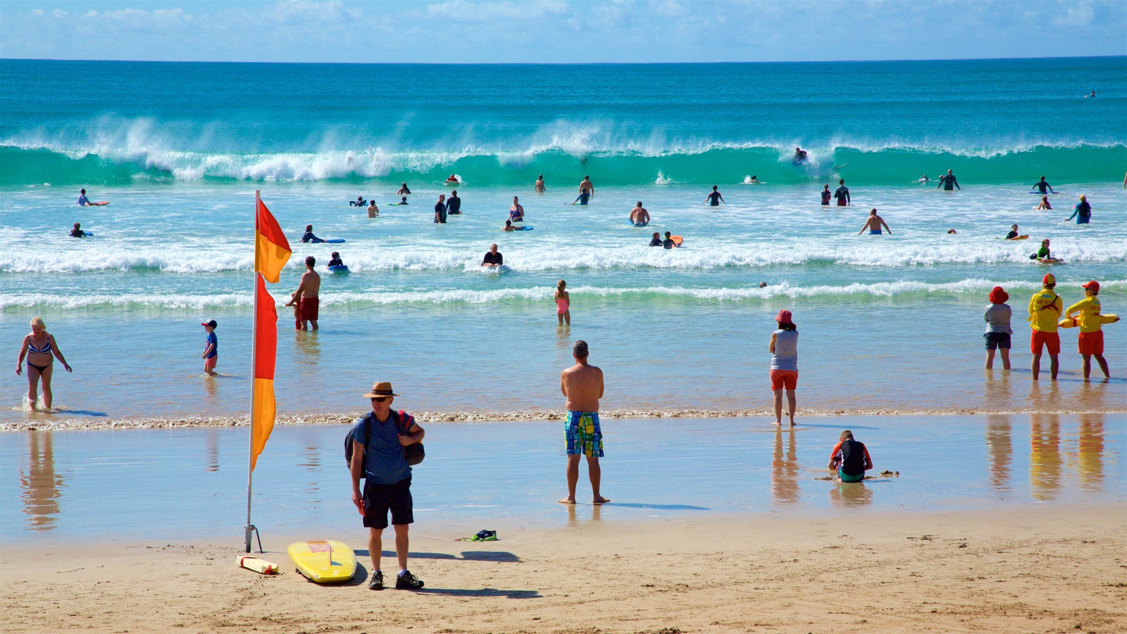 A crowded beach with people surfing and swimming in the ocean.
