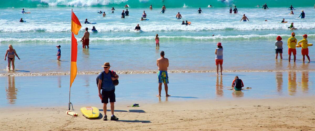 A crowded beach with people surfing and swimming in the ocean.