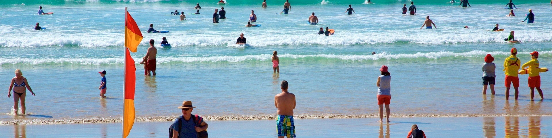 A crowded beach with people surfing and swimming in the ocean.