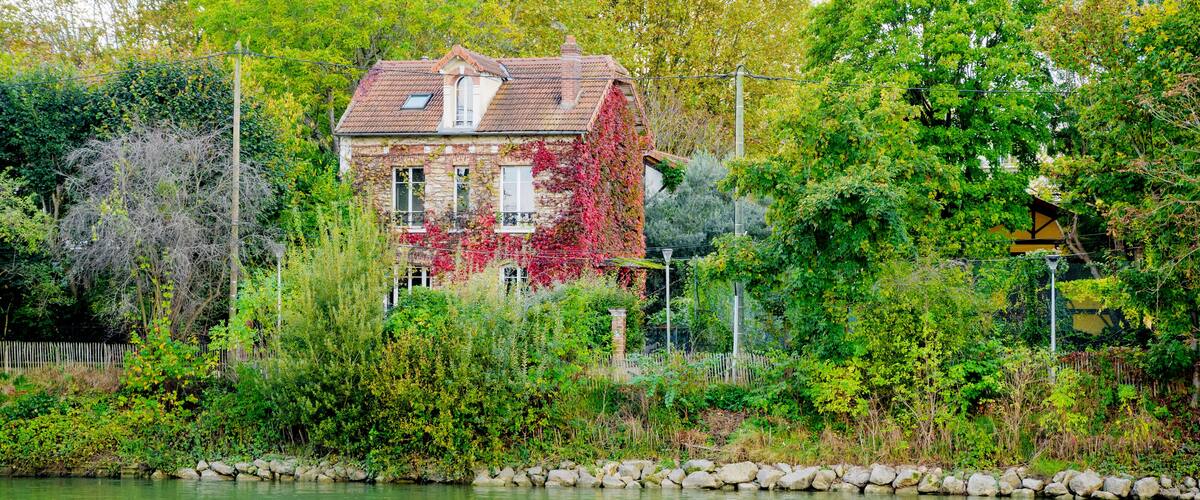 Een huis met rode klimop, omringd door weelderige begroeiing en een rustige rivier.