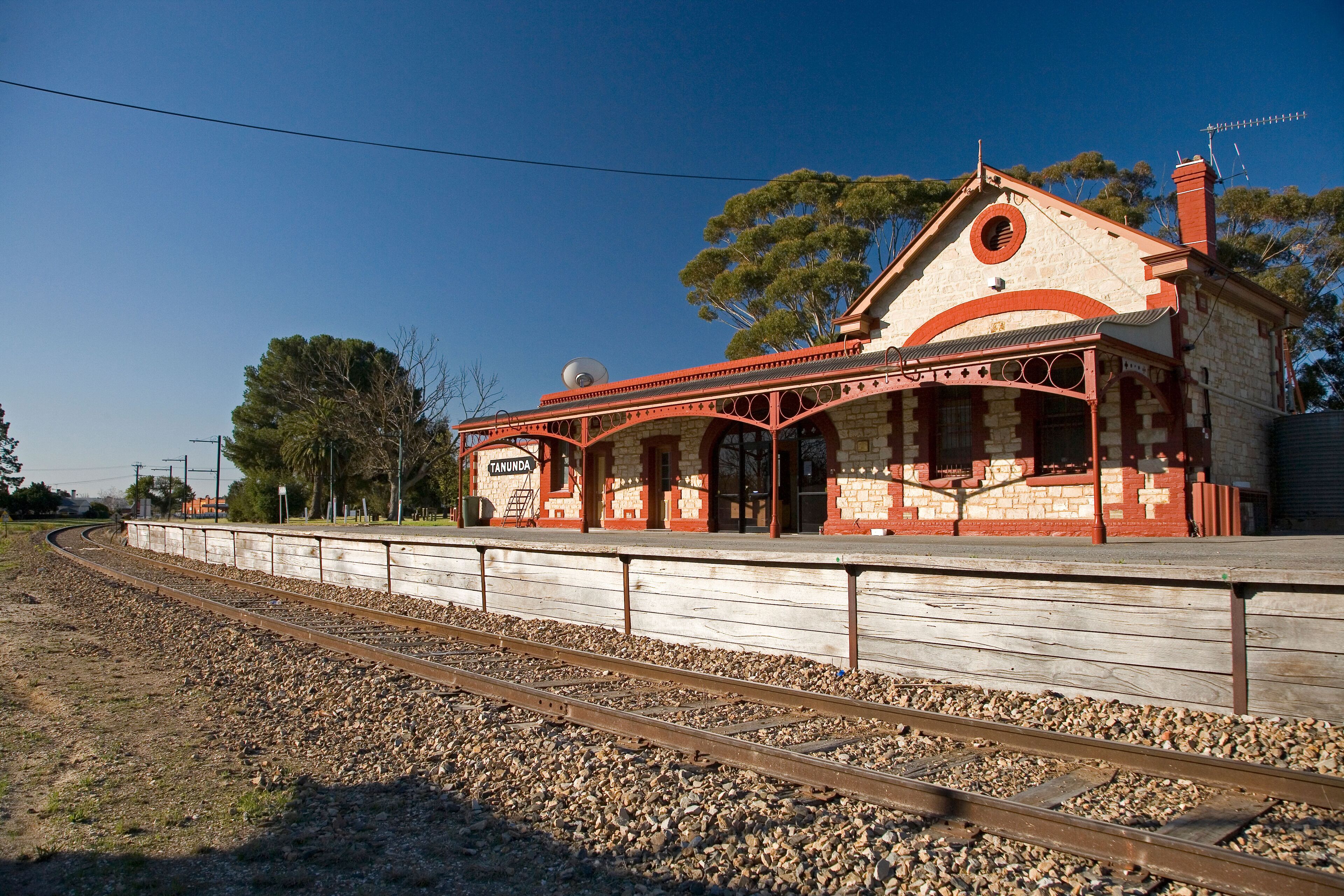 A historic train station with a distinctive red and white facade, surrounded by gravel and railway tracks.