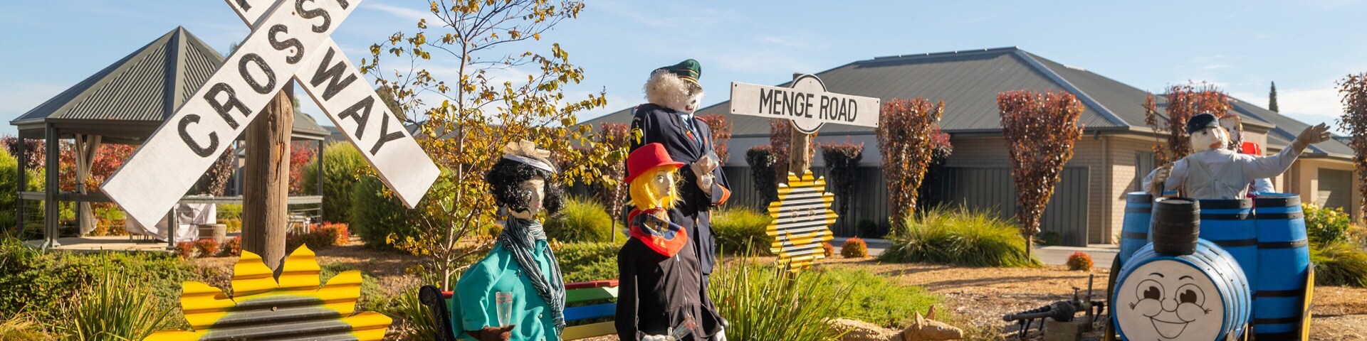Un jardín con un cartel de 'Railroad Crossing', un banco y un cartel de 'Menge Road'.