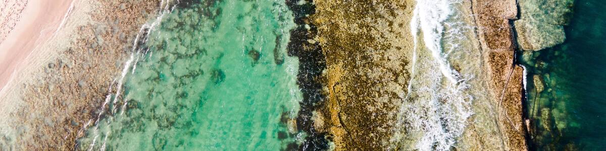 An aerial view of a beach with clear turquoise waters, a sandy shore, and rocky outcrops.