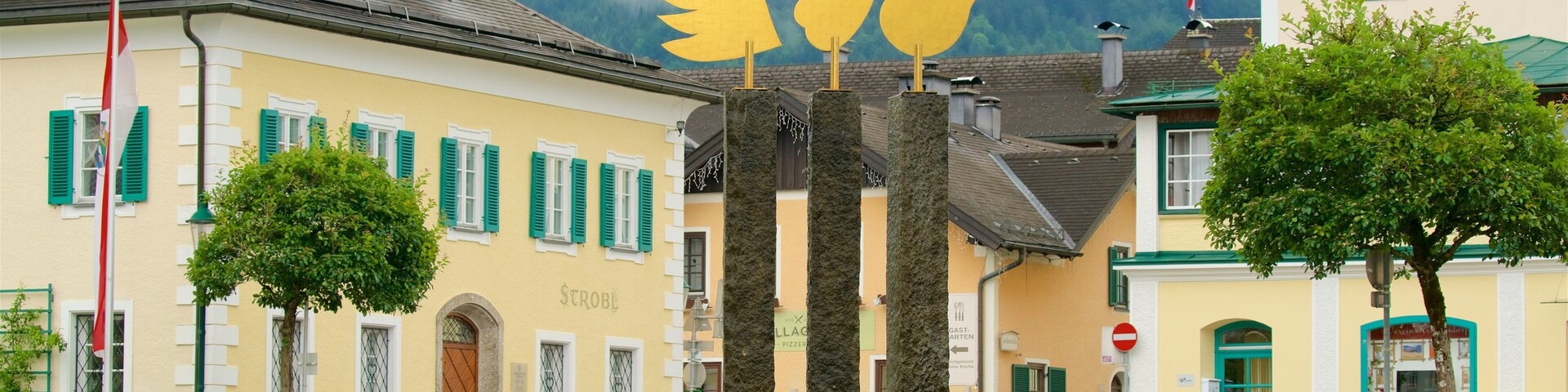 A town square with a fountain, benches, and buildings with green shutters.