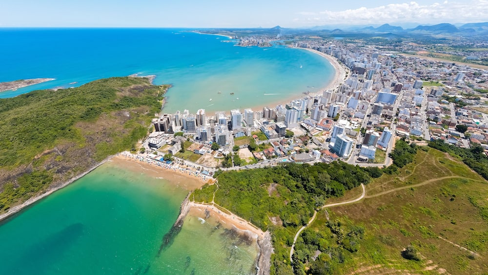 Imagem aérea de drone da Praia do Morro em um dia ensolarado, com pessoas passeando, praticando esportes e descansando ao sol. Cidade de Guarapari no Espírito Santo