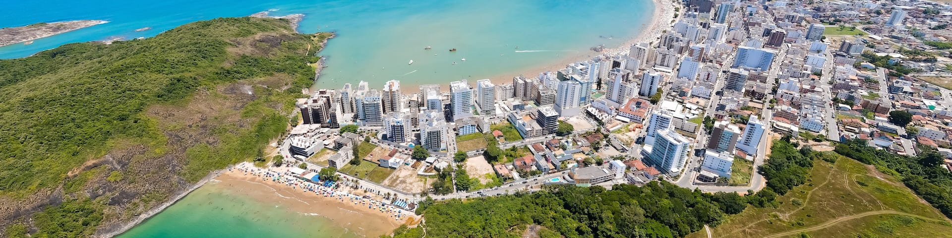 Imagem aérea de drone da Praia do Morro em um dia ensolarado, com pessoas passeando, praticando esportes e descansando ao sol. Cidade de Guarapari no Espírito Santo