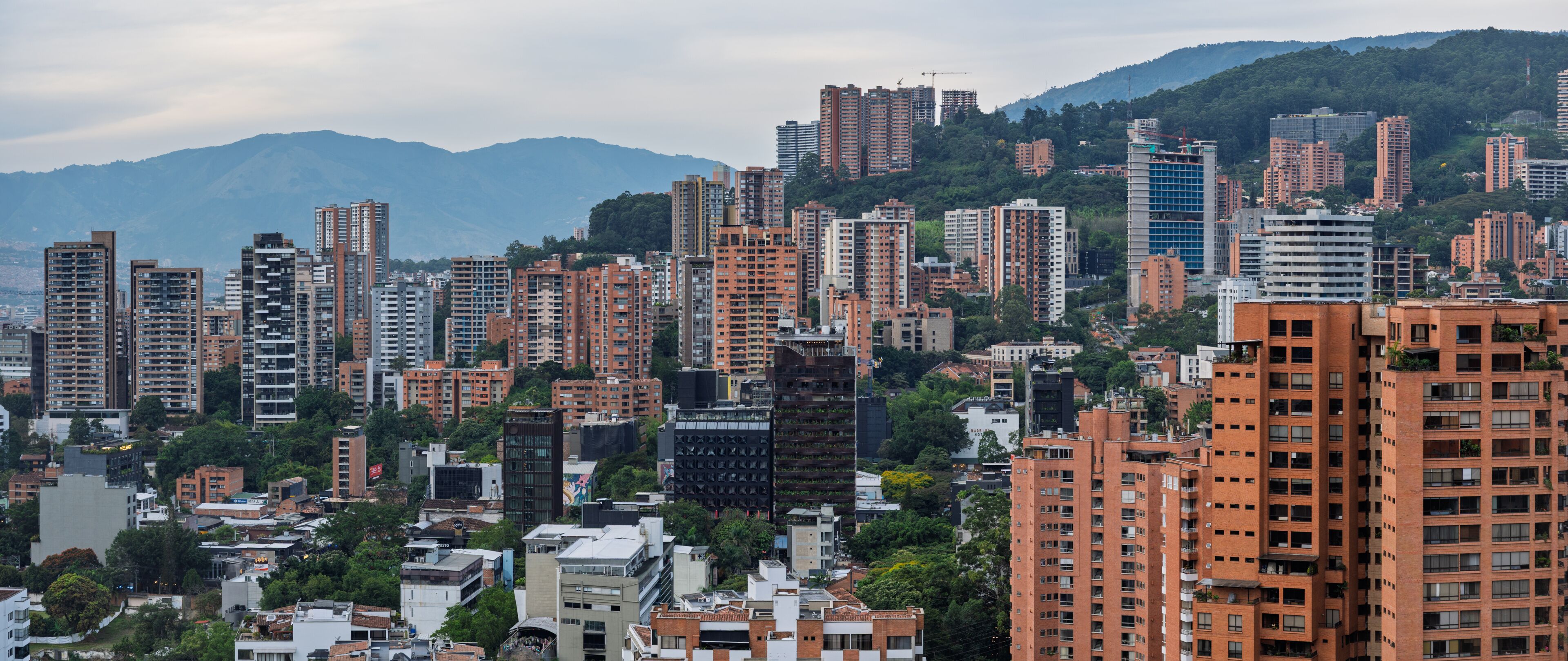 A densely packed urban area with high-rise buildings, a mix of residential and commercial structures, and a backdrop of mountains.