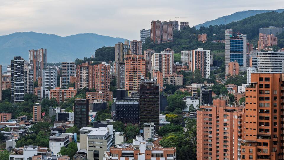 A densely packed urban area with high-rise buildings, a mix of residential and commercial structures, and a backdrop of mountains.
