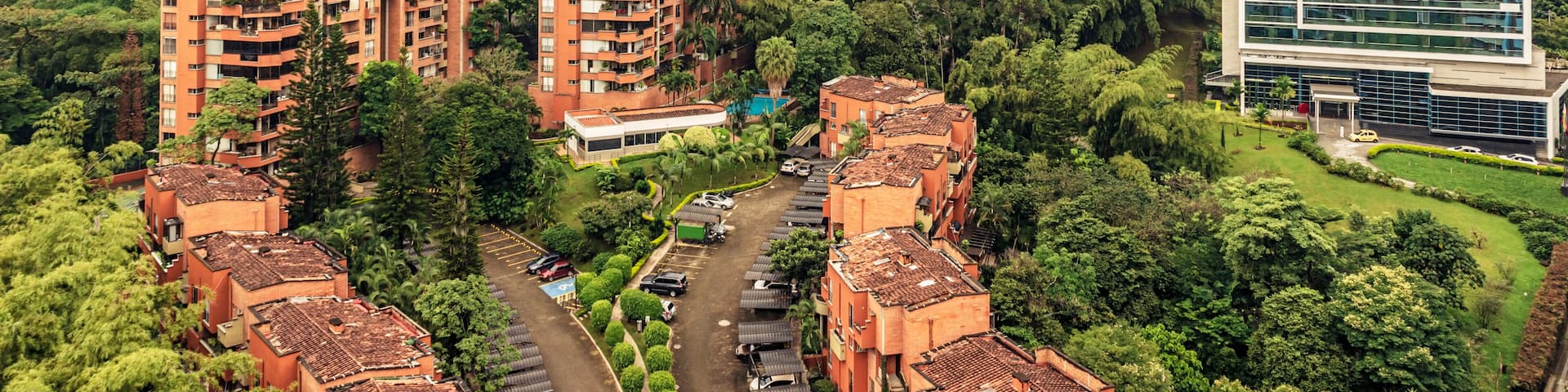 A cityscape with high-rise buildings, lush greenery, and a mountain range in the background.