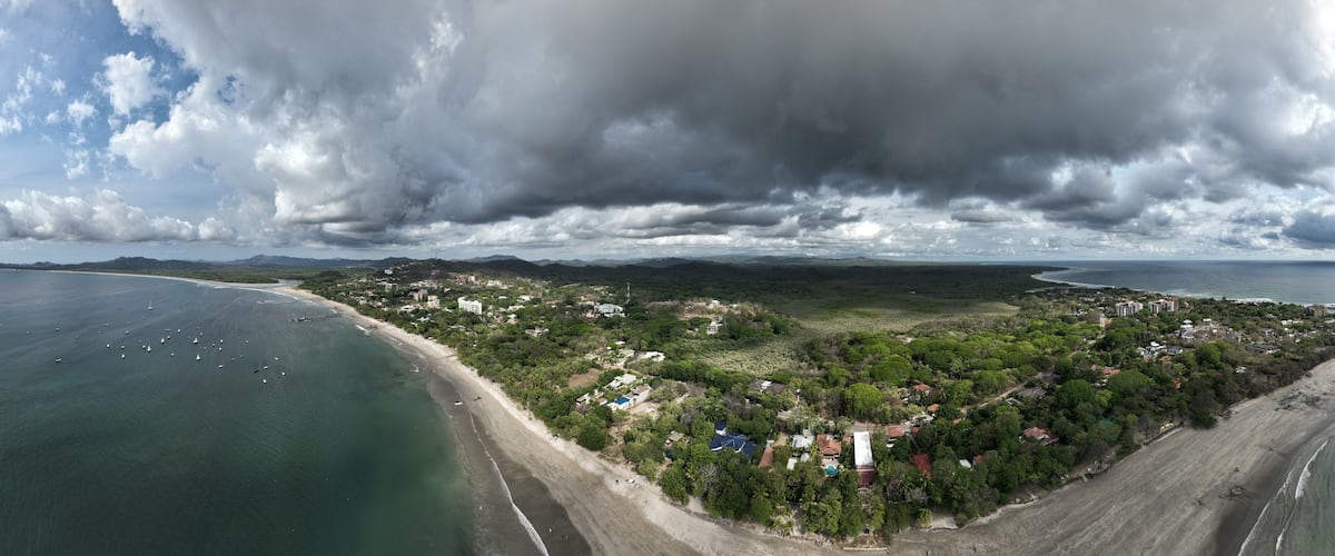 An aerial view of a coastal town with a beach, houses, and mountains in the background.