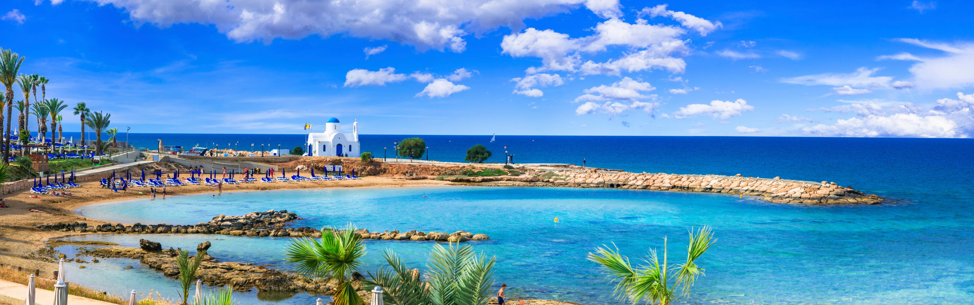 A coastal resort with a clear blue sea, a white church, and palm trees.