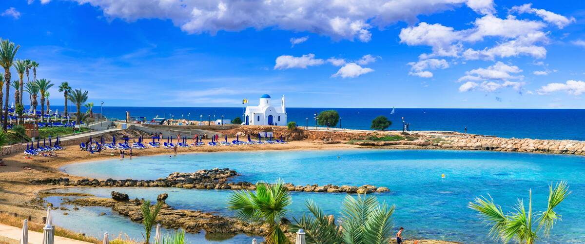 A coastal resort with a clear blue sea, a white church, and palm trees.
