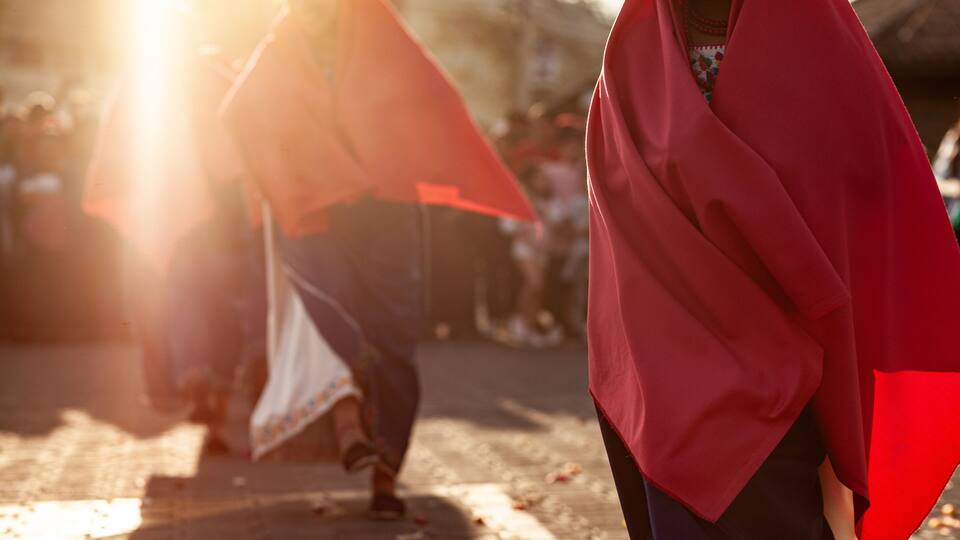 A person with a red shawl walking on a sunlit street.