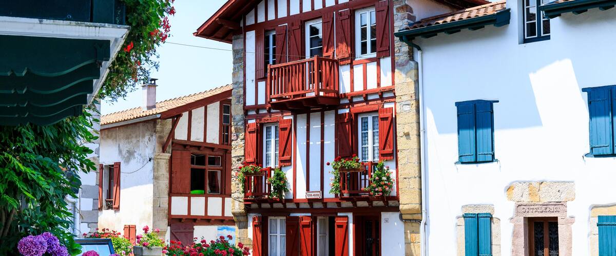 A traditional European building with red shutters, white walls, and a balcony with potted plants.