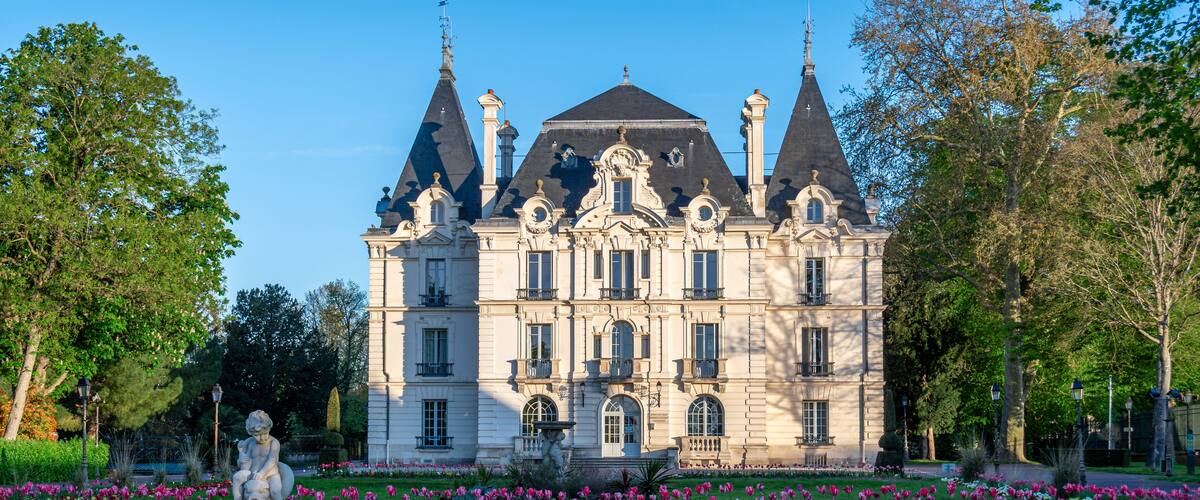 A grand historic building with ornate architecture, surrounded by a vibrant flower garden and statues.