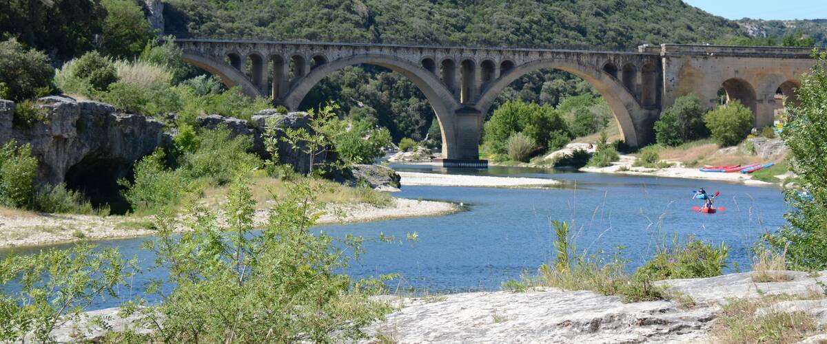 A stone bridge over a river with a kayaker in the water.
