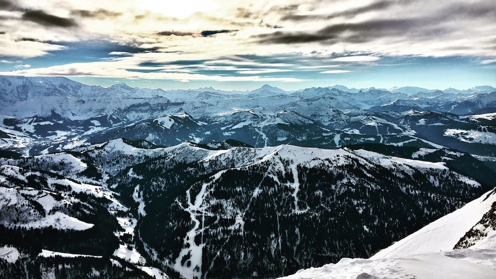Une chaîne de montagnes enneigées, avec une vallée et des sommets lointains, sous un ciel nuageux.
