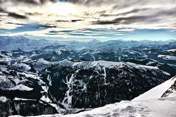Une chaîne de montagnes enneigées, avec une vallée et des sommets lointains, sous un ciel nuageux.