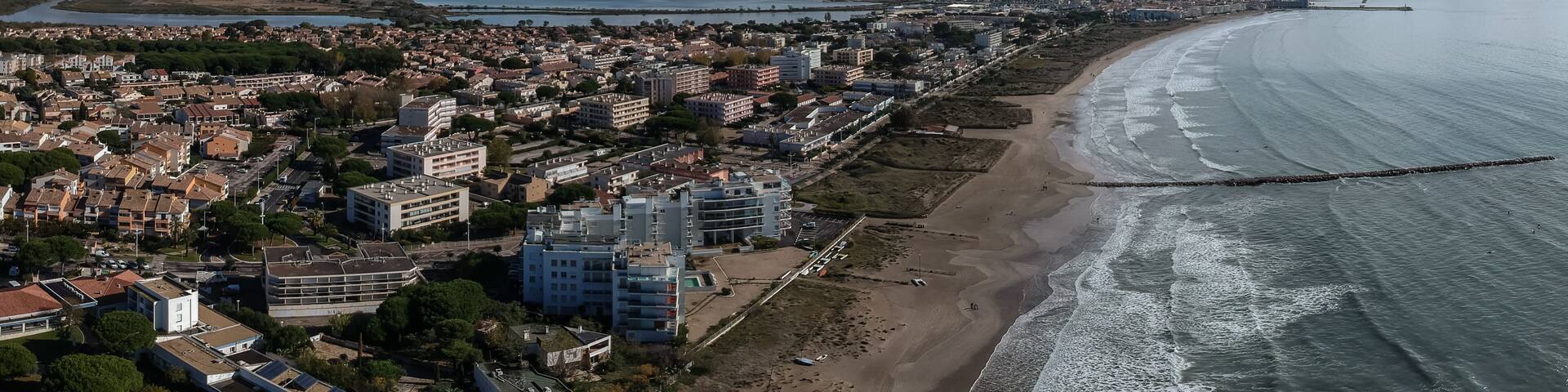 A coastal cityscape with a beach, residential buildings, and a bridge.