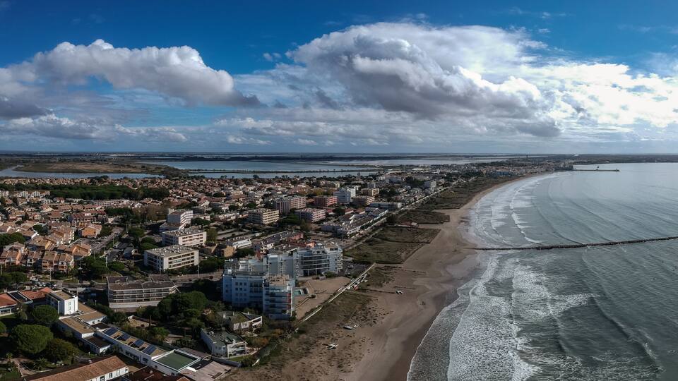 A coastal cityscape with a beach, residential buildings, and a bridge.