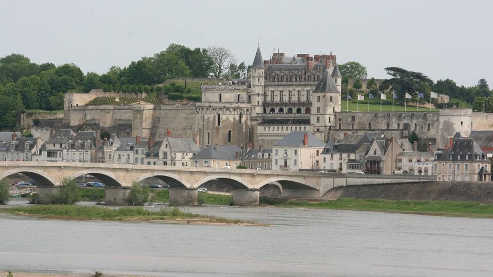 A historic stone bridge over a river, leading to a castle with multiple towers and a fortified wall.