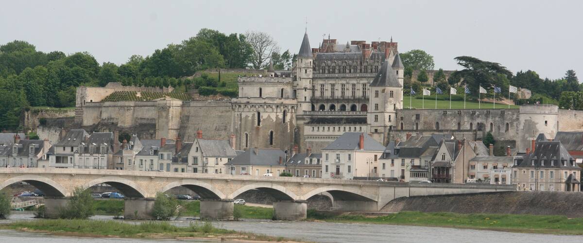 A historic stone bridge over a river, leading to a castle with multiple towers and a fortified wall.