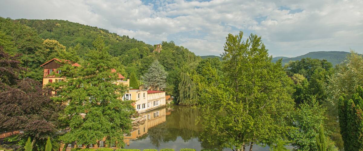 A serene riverside landscape with lush greenery, a reflective water body, and traditional buildings nestled among the trees.