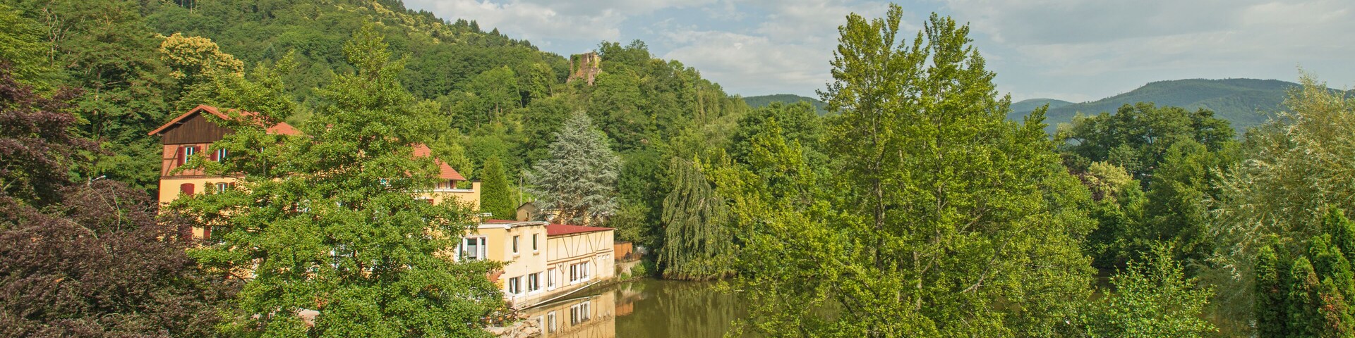 A serene riverside landscape with lush greenery, a reflective water body, and traditional buildings nestled among the trees.
