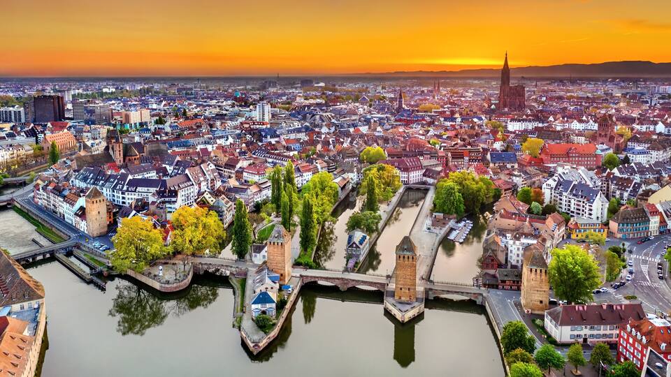 A panoramic view of a city with a river, bridges, and historic buildings during sunset.