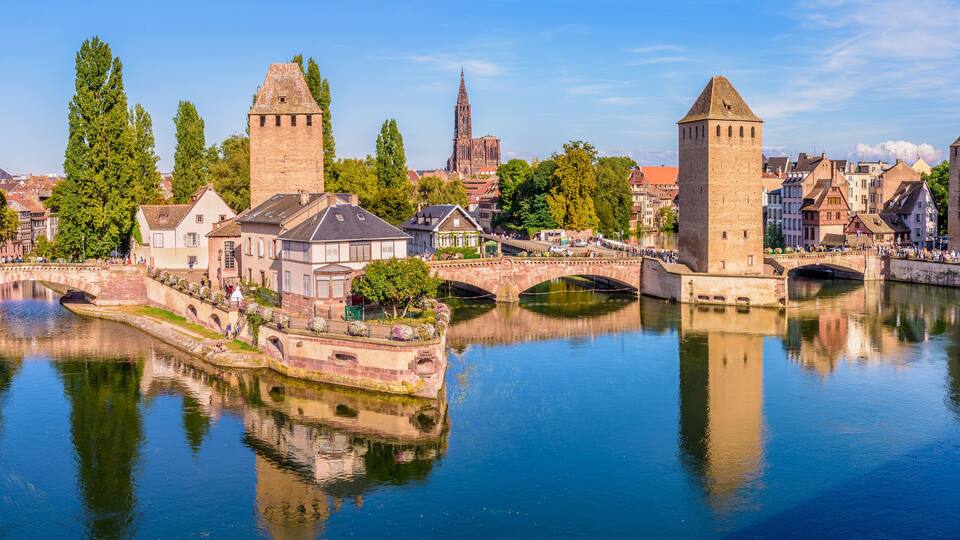 A river with bridges, historic buildings, and towers reflecting in the water.