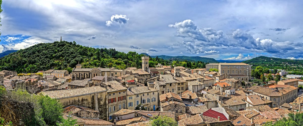 A historic town with dense architecture, a prominent tower, and lush green hills in the background.