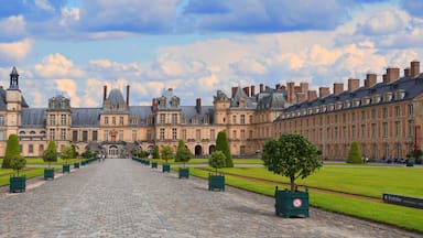A grand courtyard with a central cobblestone path, surrounded by symmetrical buildings with classical architecture.