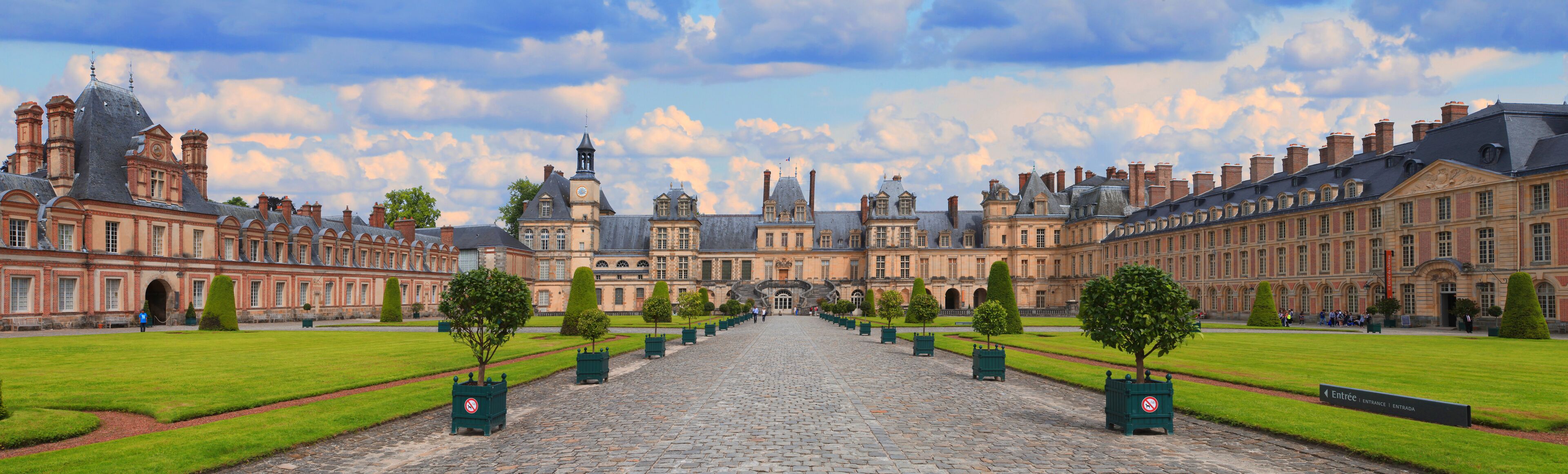 A grand courtyard with a central cobblestone path, surrounded by symmetrical buildings with classical architecture.
