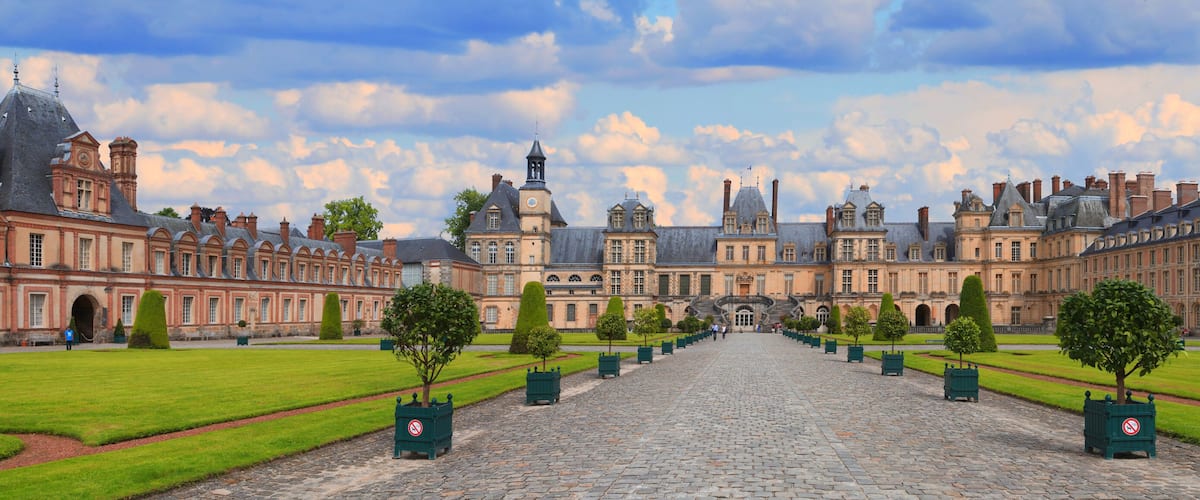 A grand courtyard with a central cobblestone path, surrounded by symmetrical buildings with classical architecture.