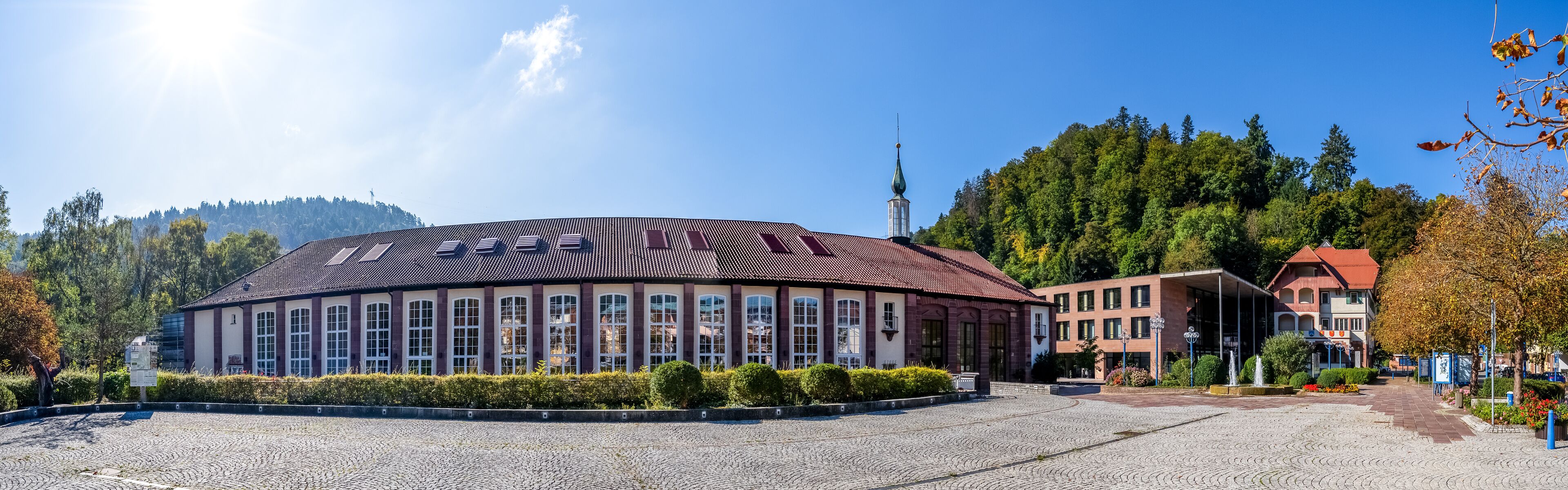 A historic building with a tiled roof, surrounded by cobblestone pavement and lush greenery.