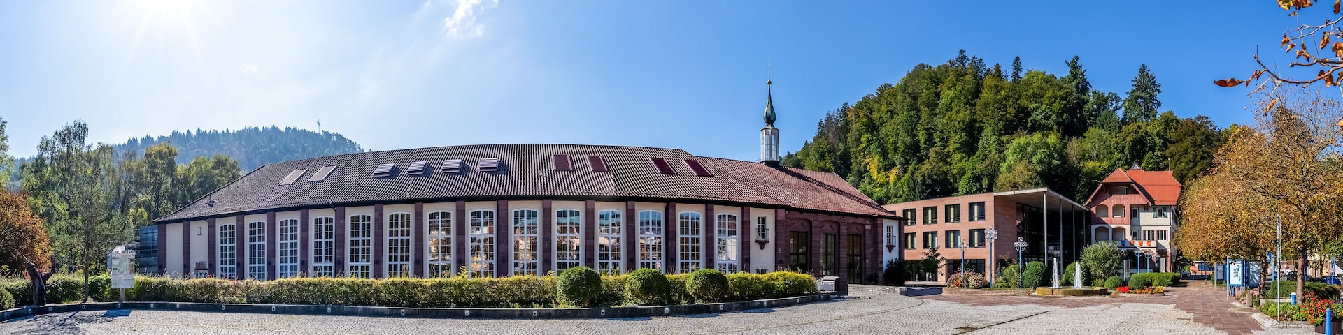A historic building with a tiled roof, surrounded by cobblestone pavement and lush greenery.