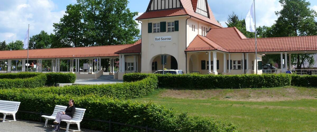 A historic building with a clock tower, named Bad Saarow, surrounded by lush greenery and a clear sky.