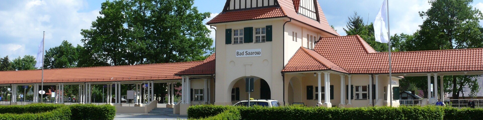 A historic building with a clock tower, named Bad Saarow, surrounded by lush greenery and a clear sky.