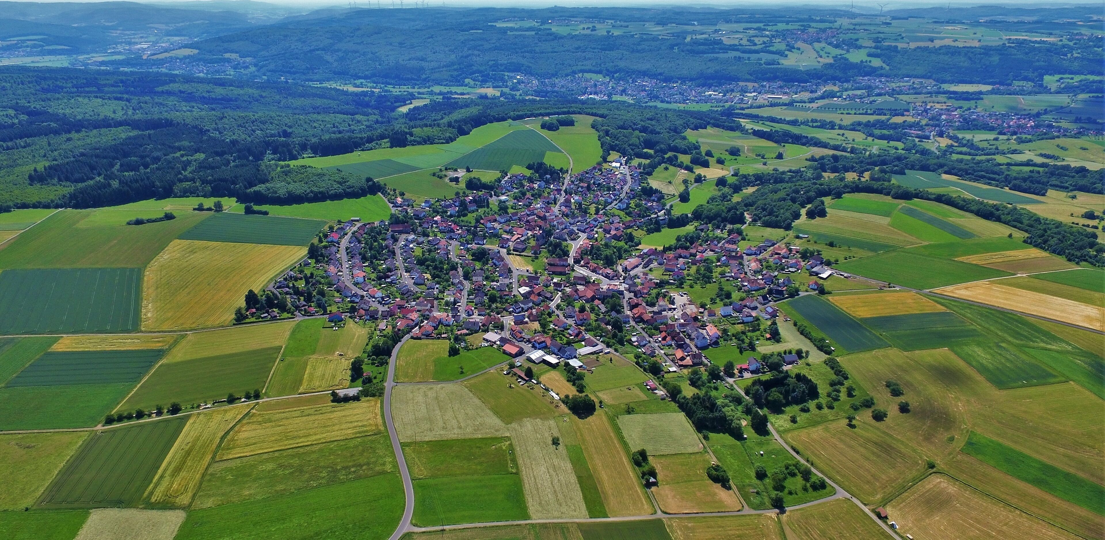An aerial view of a rural village surrounded by fields and forests.