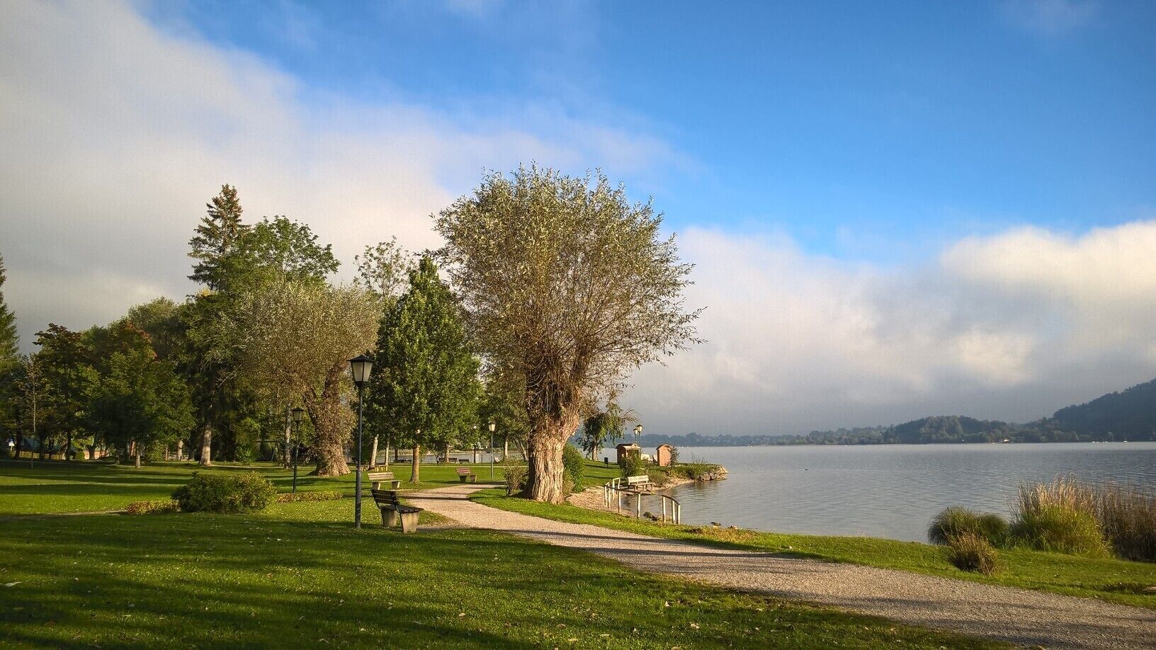 A park with a lake, benches, trees, and a clear sky.
